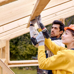 contractors in work wear using electric drill. Home renovation, sustainable living, building cottage house. Building Technologies. Industrial Theme. Two builders in uniform and hardhat work as team
